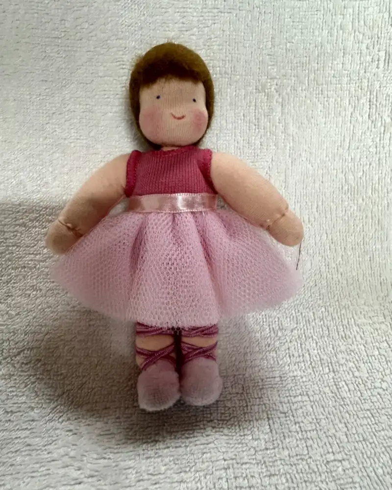 Bailarina de pé sobre manta branca, de frente, com collant pink, faixa de cetim rosa e saia de tule rosa