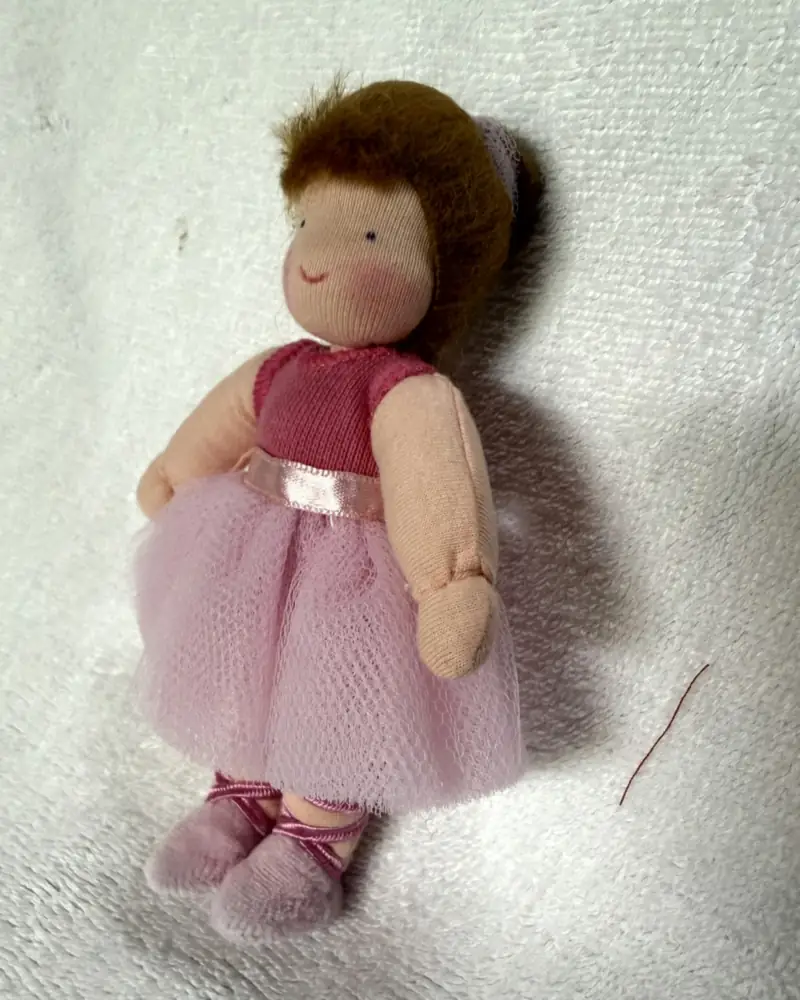 Bailarina vista de lado, com cabelo curto castanho-acobreado, coque na nuca e sapatilhas de fitas trançadas