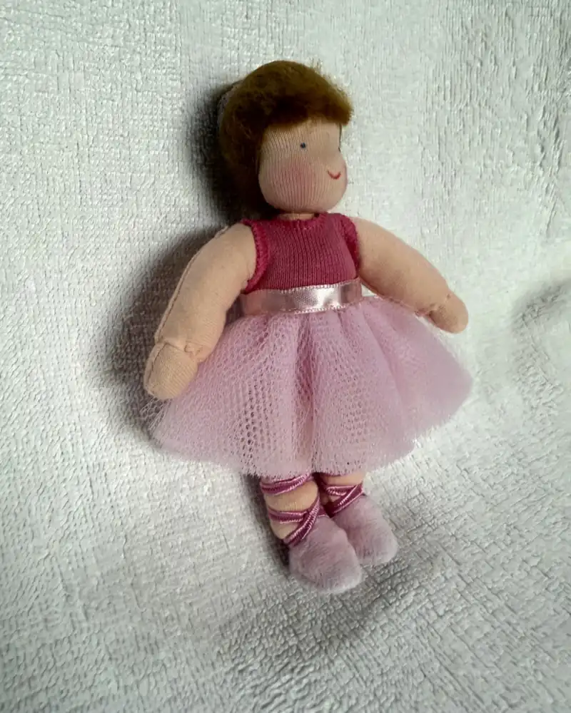 Bailarina em ângulo, com os braços junto à saia de tule rosa e as fitas pink trançadas nas pernas