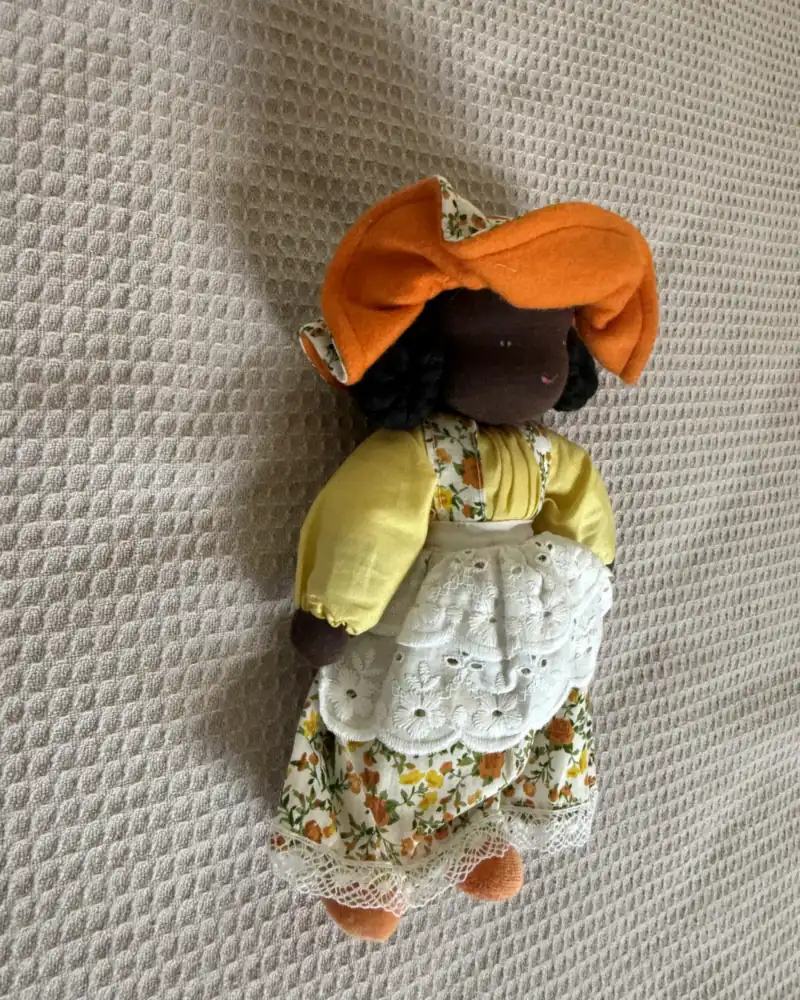 Chapeuzinho de pele negra vista de frente, com cachos pretos, saia de florzinhas e sapatinhos laranja