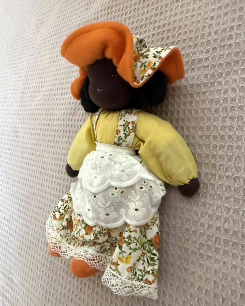 Chapeuzinho vista de perto, com touca laranja de forro florido, blusa amarela e avental branco vazado