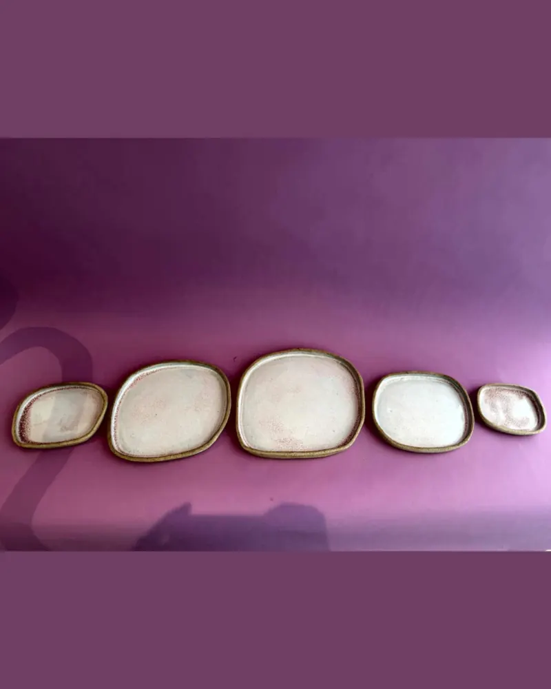 Travessas do conjunto lado a lado, em tamanhos diferentes e formato quadrado arredondado, sobre fundo roxo