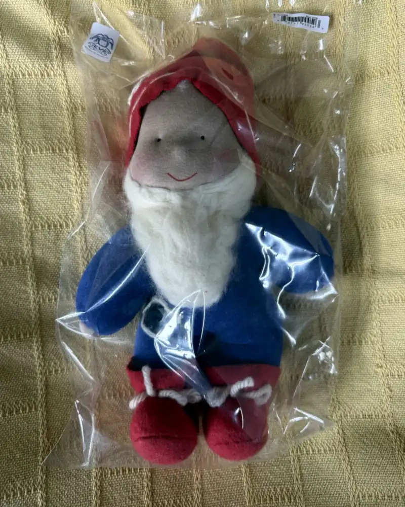 Gnomo de roupa azul no saquinho, com detalhe escuro contornado de branco no peito e botinhas vermelhas