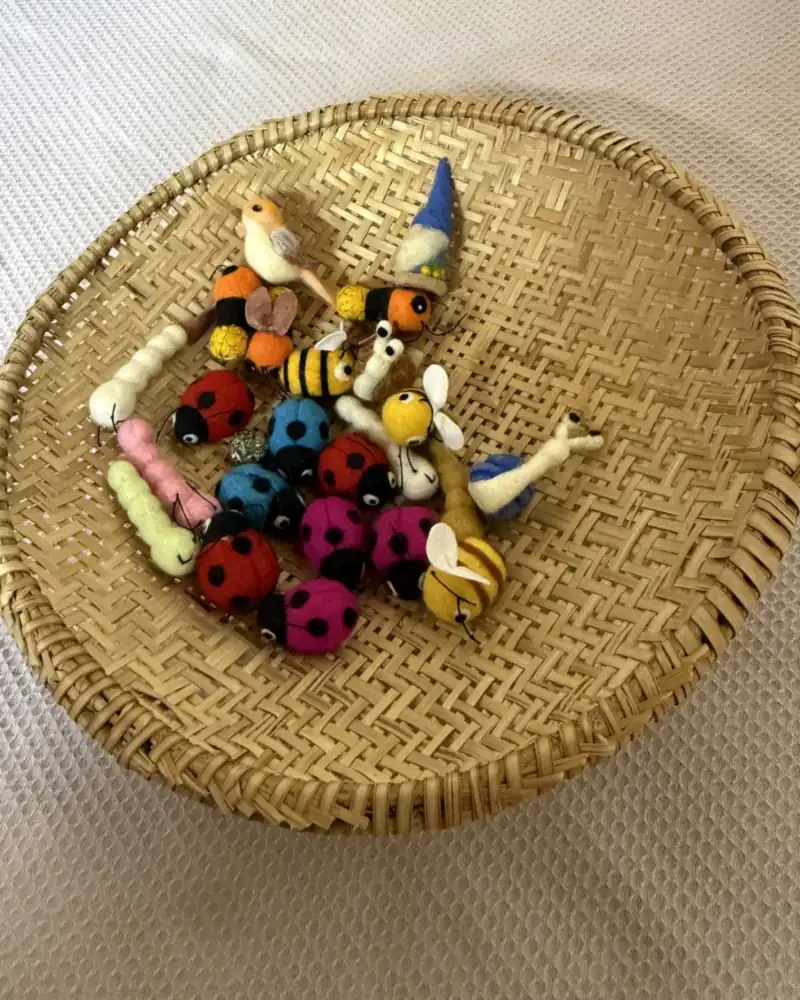 Miniaturas de feltro num cesto de palha: passarinho, gnomo de gorro azul, abelhinhas e lagartas branca, rosa e verde