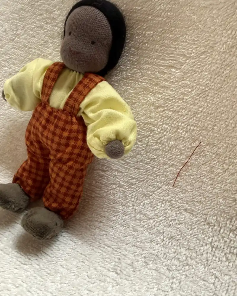 O menino de macacão xadrez visto de lado, com as mangas bufantes da blusa amarelo-clara e os pés cinza