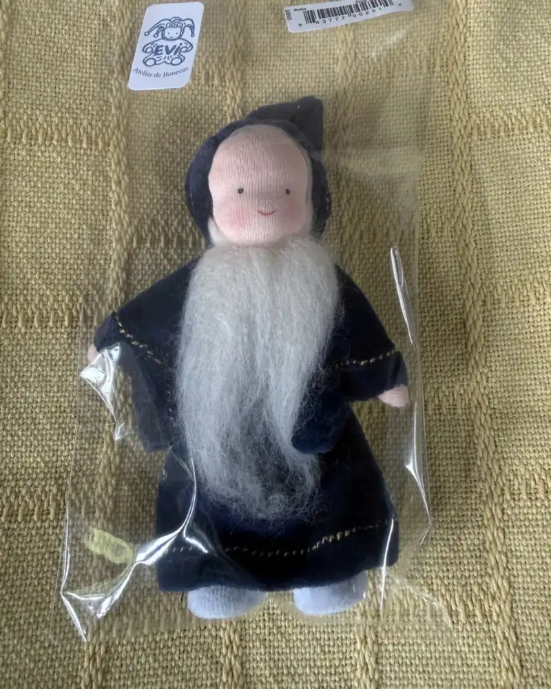 Boneco Merlin de frente no saquinho, com manto azul-marinho de pesponto dourado e pés claros