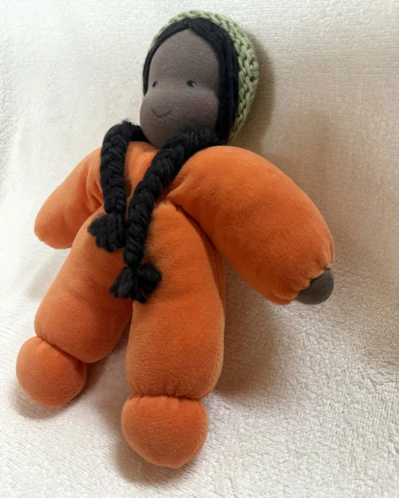 Molinha Laranja de três quartos, mostrando a touca de tricô verde-clara e os pezinhos de pelúcia