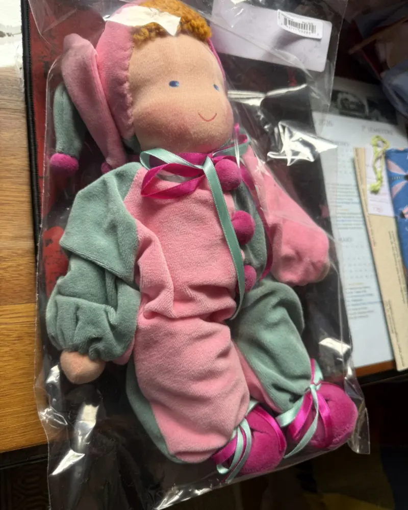 Polichinelo rosa e verde-água no saquinho, visto de perto, com gorro rosa de pontas e pés pink amarrados com fitas