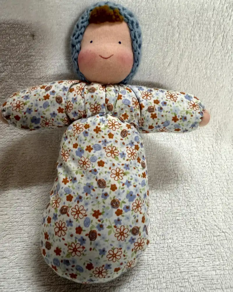 Primeira Boneca de frente, com corpo inteiriço de tecido estampado de florzinhas, touca azul e topete caramelo
