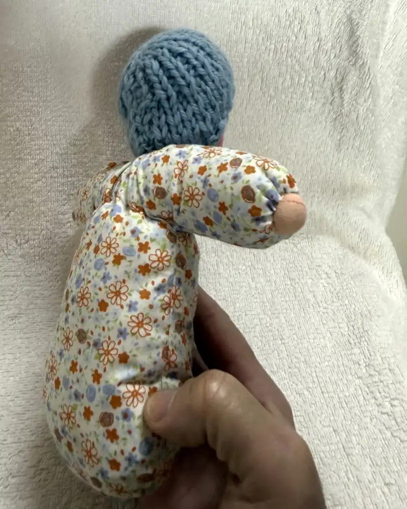 Primeira Boneca de costas na mão de um adulto, com a touca azul à mostra