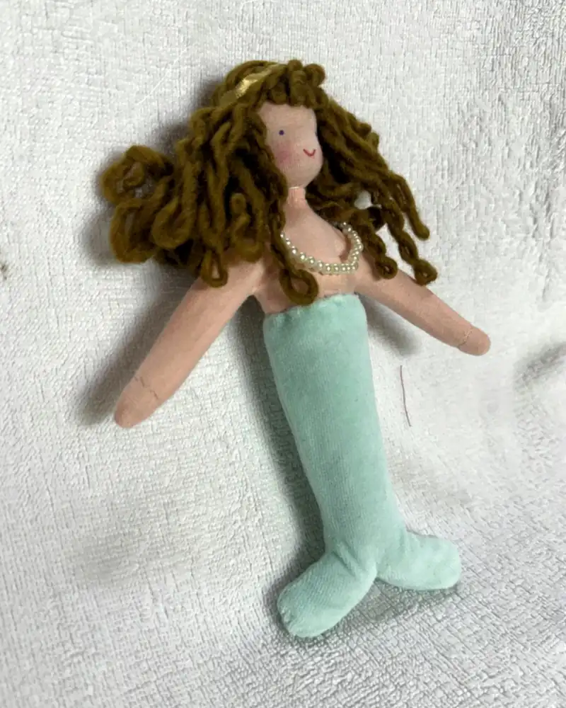 Sereia vista de perto, com tiara dourada no alto da cabeça, sorriso pequeno e cachos caramelo